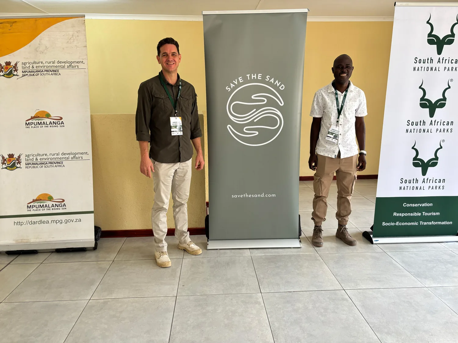 Save the Sand banner standing between provincial (DARDLEA) and national (SANParks) banners at the 2026 Arbor Day event — a bioregional platform inside the public apparatus