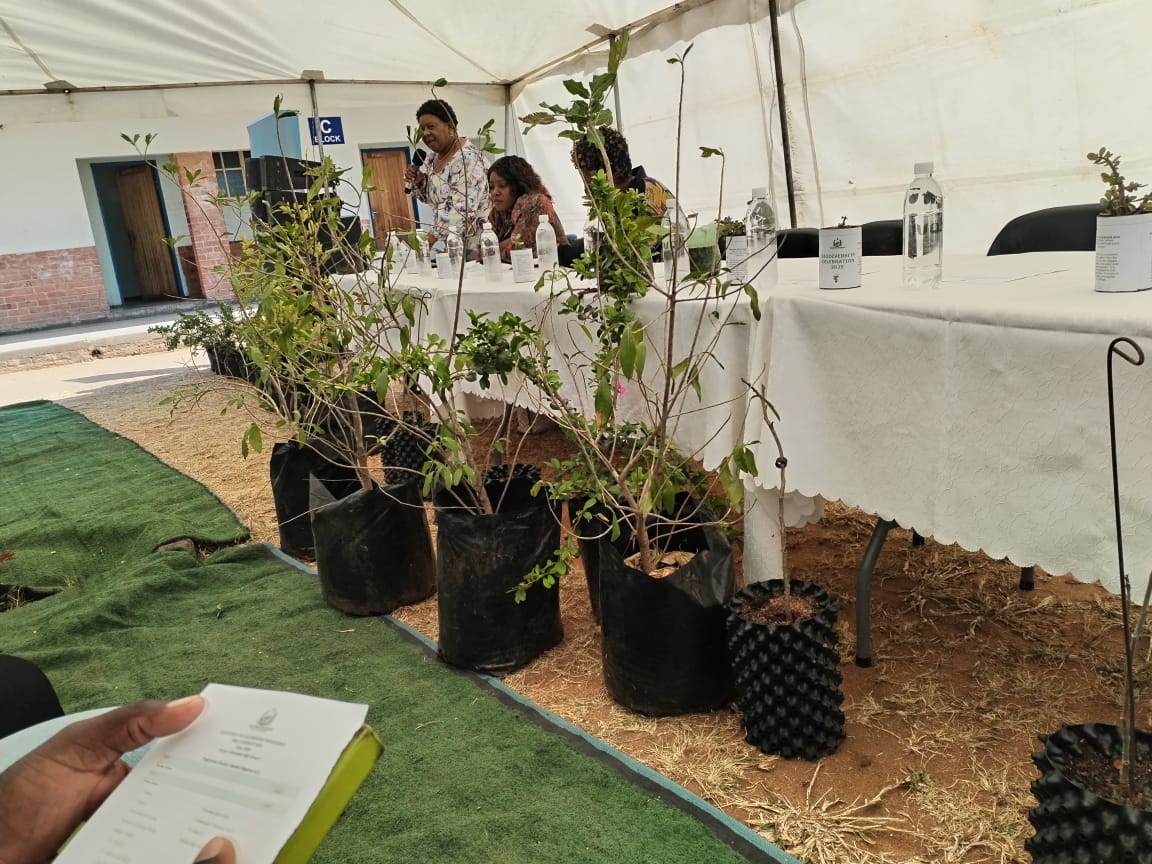 A speaker addresses learners and teachers under the awareness tent.