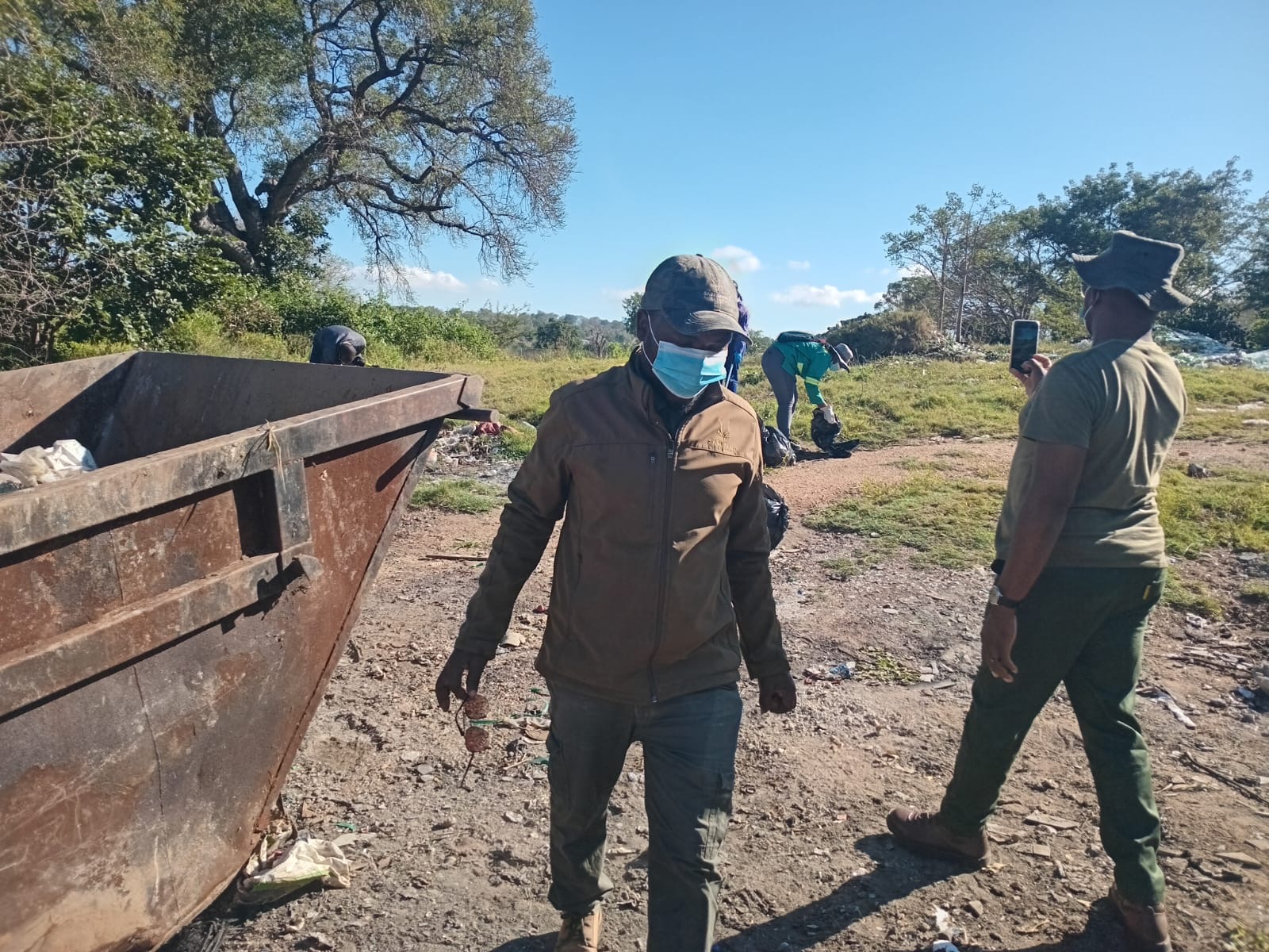 Volunteers working at an illegal dumping site, skip in foreground.