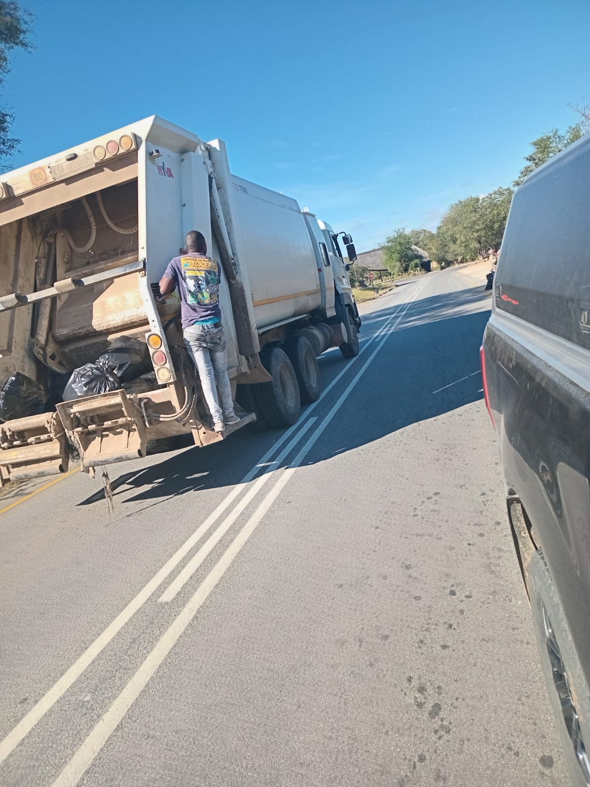 The waste truck on the road, a volunteer working at the back.