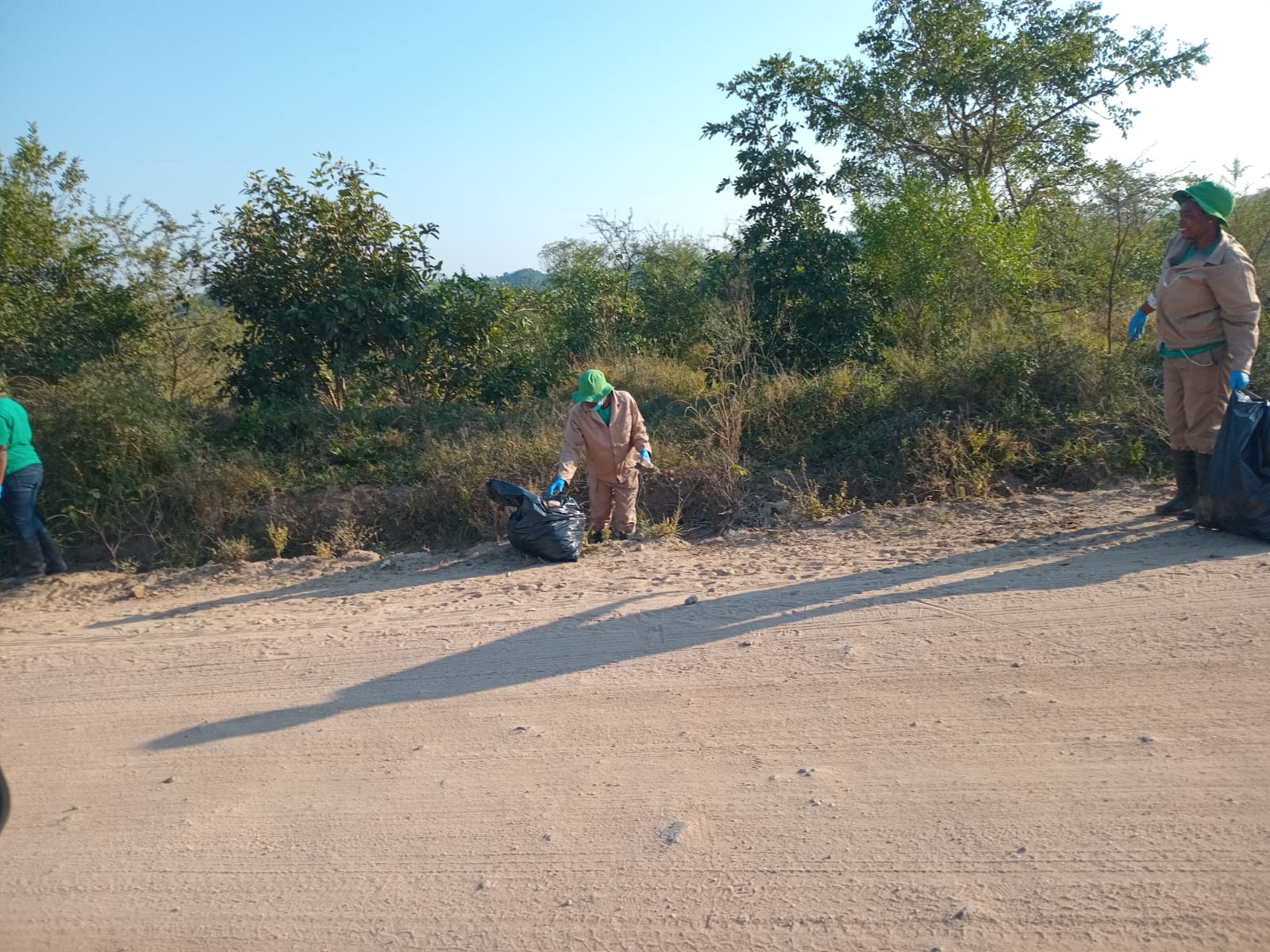A worker collecting waste from the roadside in early light.