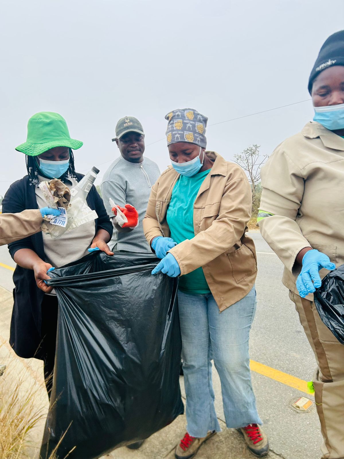 Gloved and masked volunteers holding open a collection bag along the road.