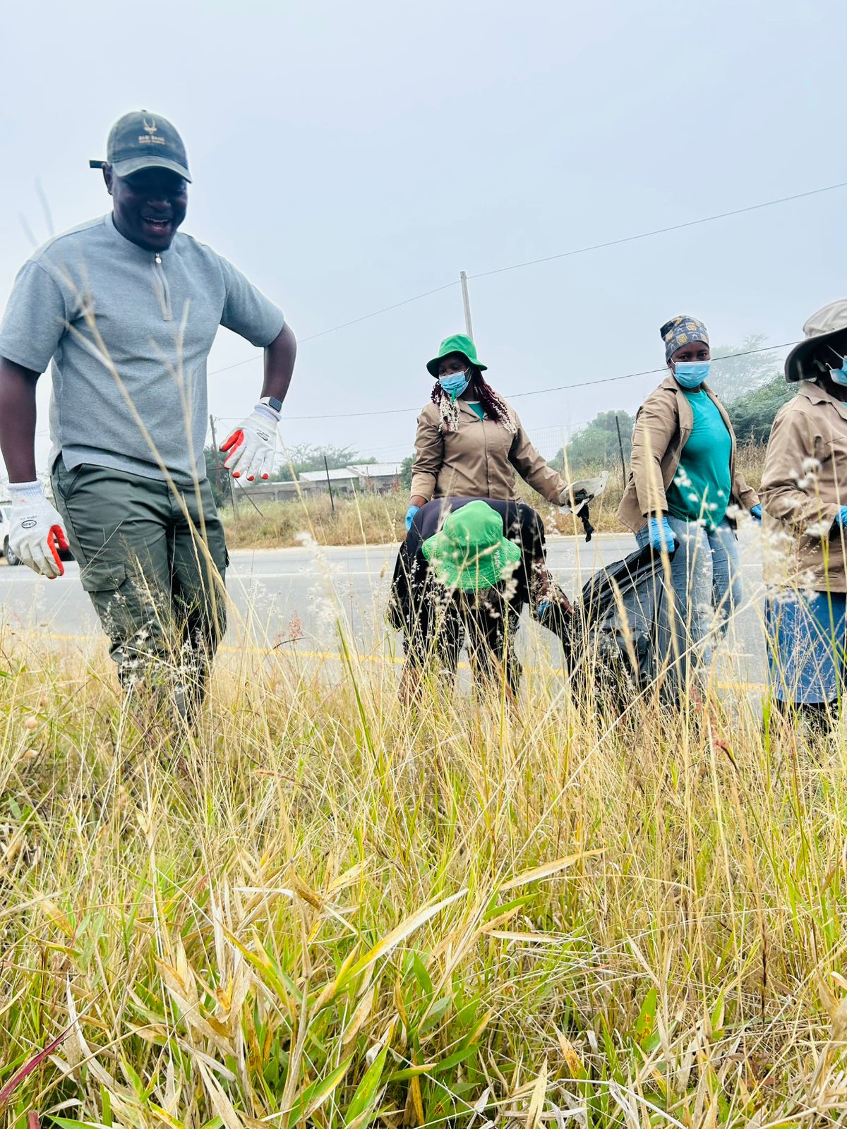 A volunteer wading into the grass to reach scattered waste, the team working behind.