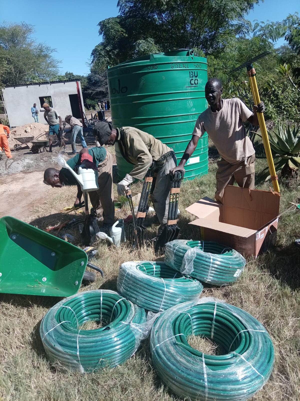 Tiyimeleni Nursery operators unpack new irrigation hosepipes and infrastructure beside a water tank.